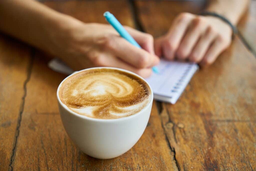 一個人一邊在一杯咖啡旁邊的筆記本上寫字，一邊練習健康的睡眠習慣。