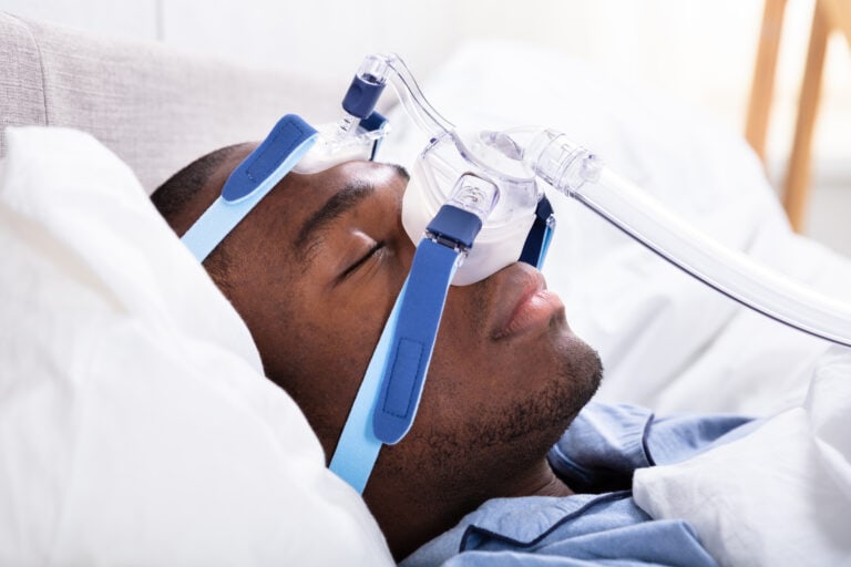 High Angle View Of A Young African Man Wearing CPAP Mask Sleeping On Bed
